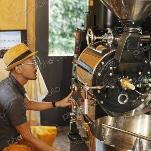 Japanese man wearing hat and glasses sitting in an Eco Cafe, operating coffee roaster… Japanese man wearing hat and glasses sitting in an Eco Cafe, operating coffee roaster…