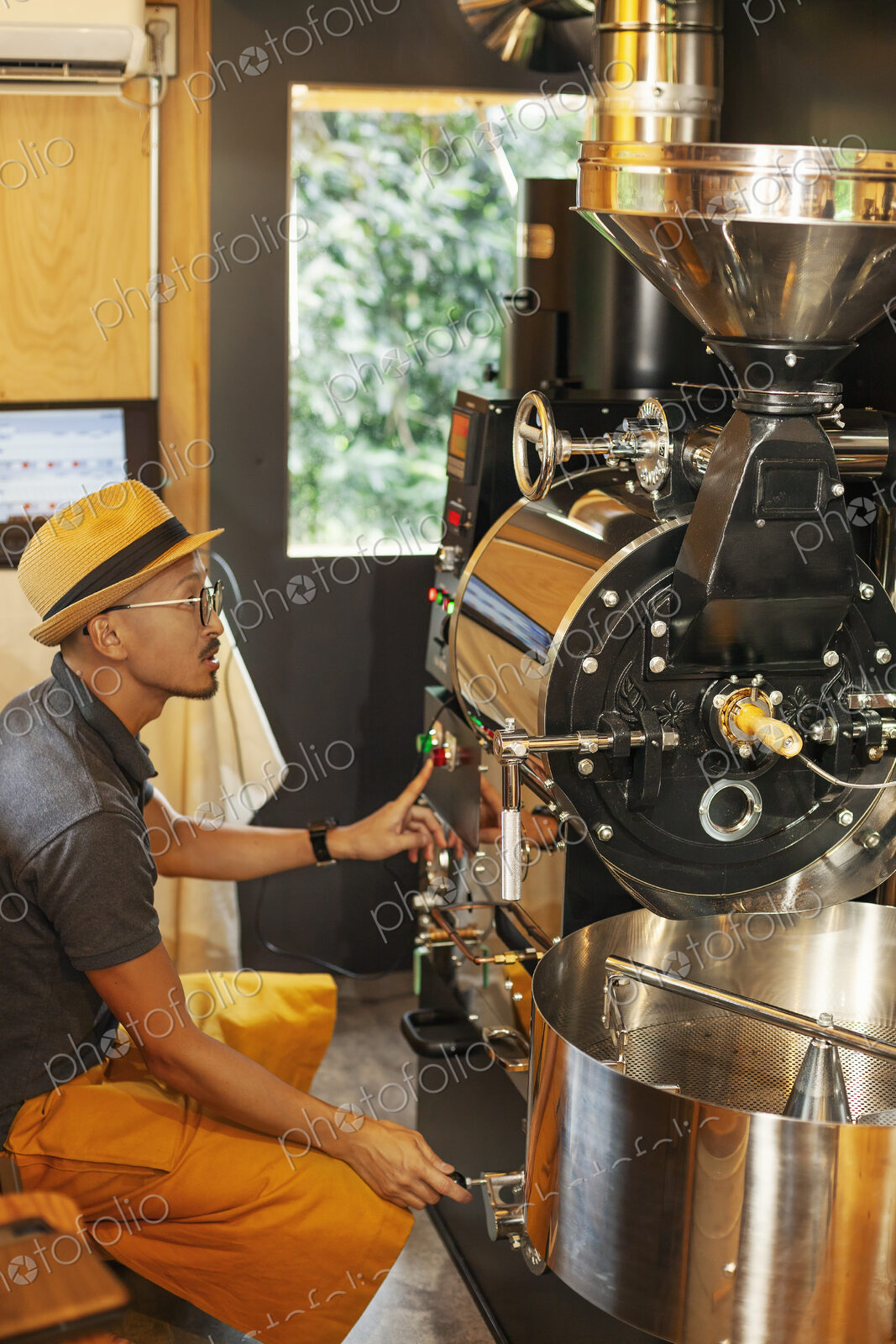 Japanese man wearing hat and glasses sitting in an Eco Cafe, operating coffee roaster…