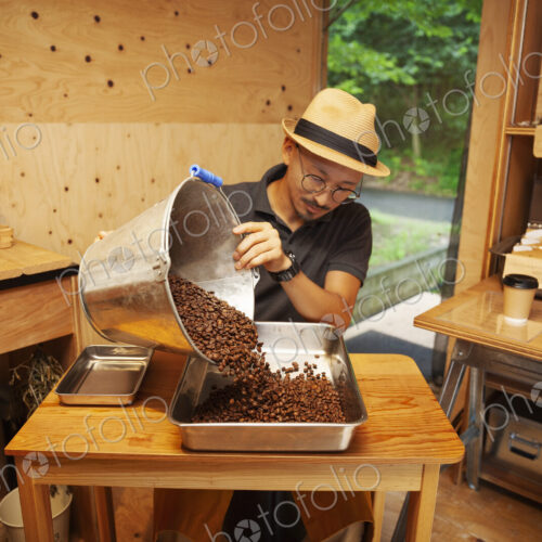 Japanese man wearing hat and glasses sitting in an Eco Cafe, pouring freshly roasted… Japanese man wearing hat and glasses sitting in an Eco Cafe, pouring freshly roasted…