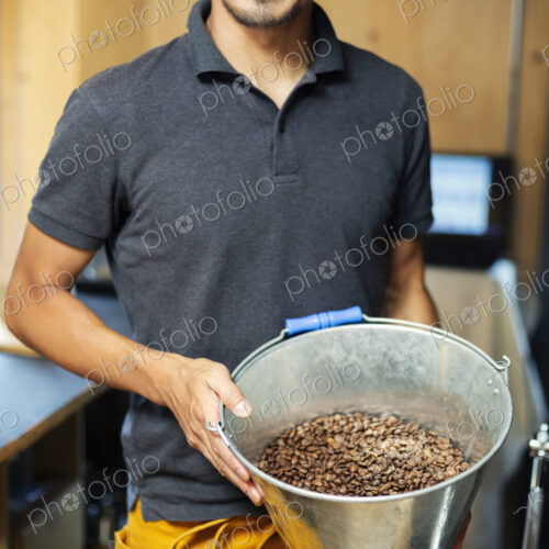 Japanese man wearing hat and glasses standing in an Eco Cafe, holding metal bucket… Japanese man wearing hat and glasses standing in an Eco Cafe, holding metal bucket…