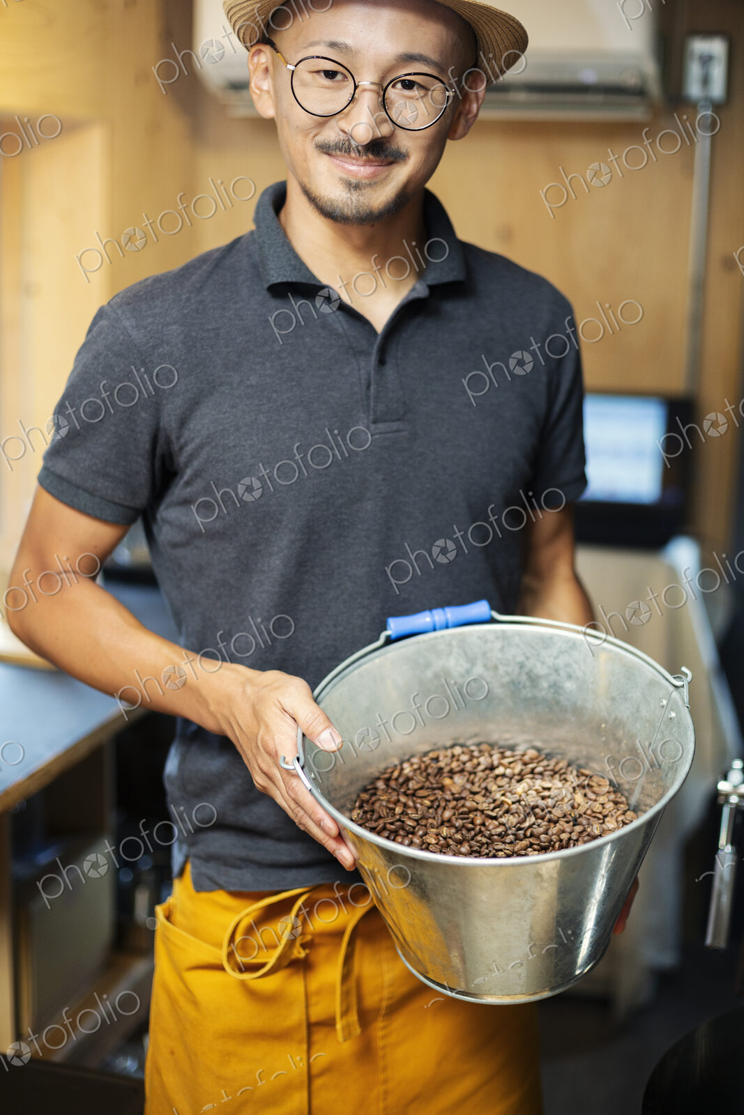 Japanese man wearing hat and glasses standing in an Eco Cafe, holding metal bucket…