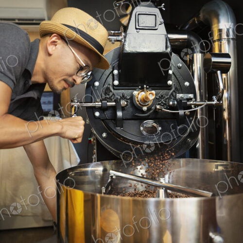 Japanese man wearing hat and glasses standing in an Eco Cafe, operating coffee roaster… Japanese man wearing hat and glasses standing in an Eco Cafe, operating coffee roaster…