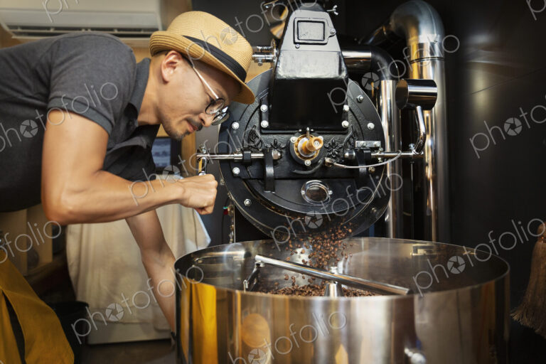 Japanese man wearing hat and glasses standing in an Eco Cafe, operating coffee roaster…