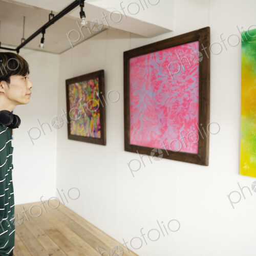 Japanese man wearing headphone looking at abstract painting in an art gallery.