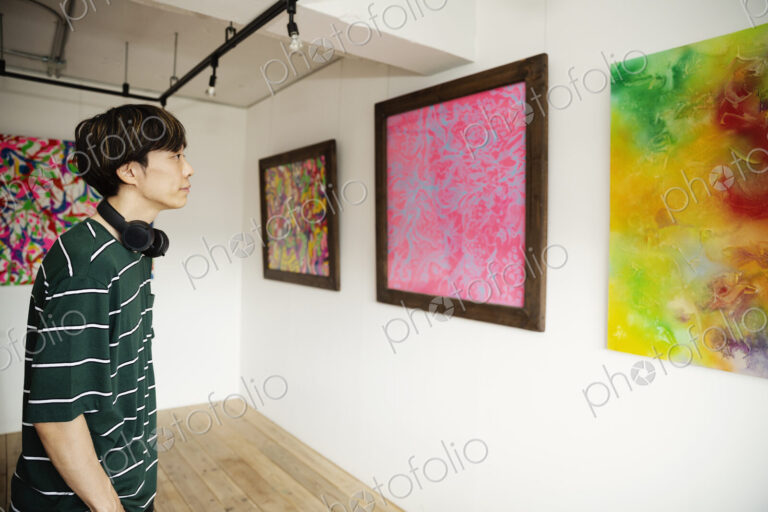 Japanese man wearing headphone looking at abstract painting in an art gallery.