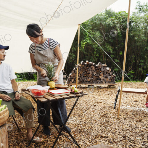 Japanese man, woman and boy gathered around a table under a canopy, preparing vegetables. Japanese man, woman and boy gathered around a table under a canopy, preparing vegetables.