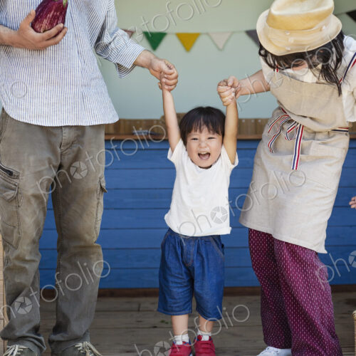 Japanese man, woman and boy standing outside a farm shop, holding hands.