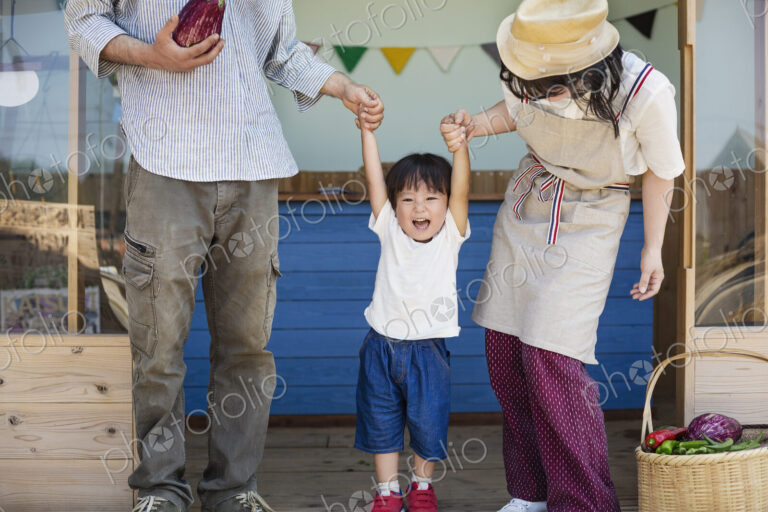 Japanese man, woman and boy standing outside a farm shop, holding hands.