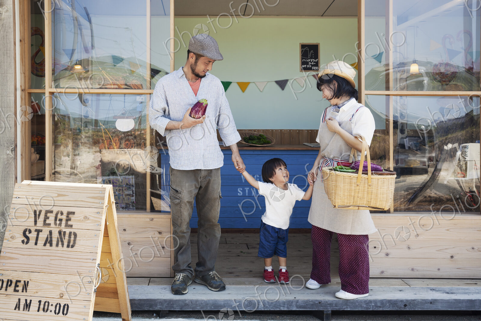 Japanese man, woman and boy standing outside a farm shop, holding hands.