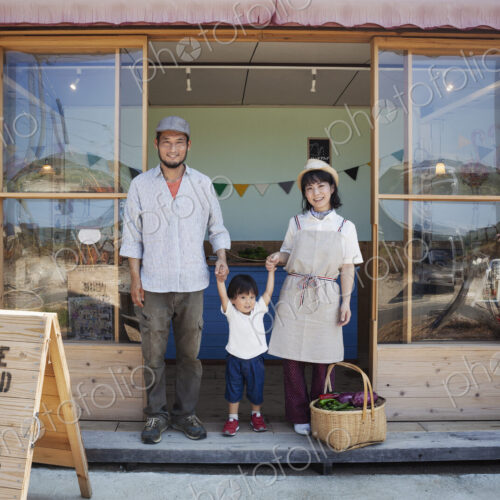 Japanese man, woman and boy standing outside a farm shop, holding hands, looking at… Japanese man, woman and boy standing outside a farm shop, holding hands, looking at…