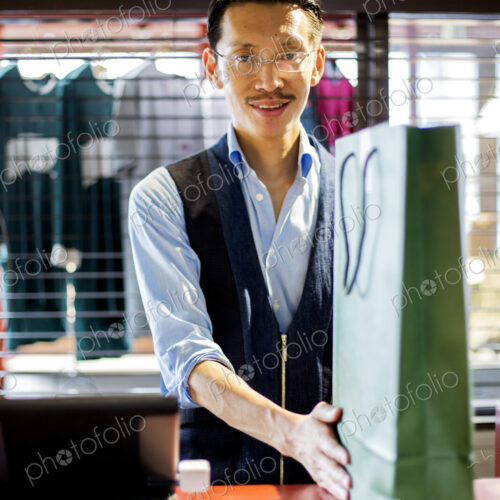 Japanese salesman in clothing store, holding green shopping bag Japanese salesman in clothing store, holding green shopping bag