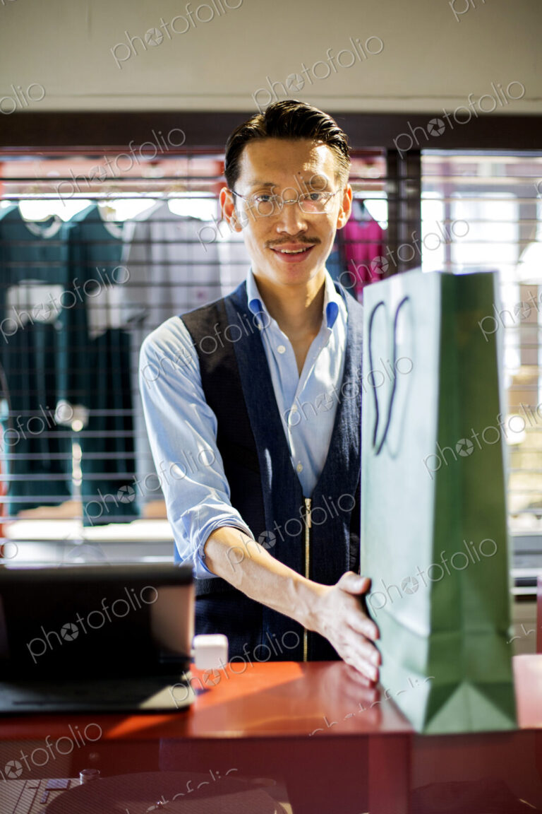 Japanese salesman in clothing store, holding green shopping bag