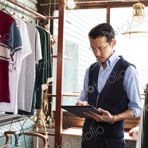 Japanese salesman standing in clothing store, looking at digital tablet. Japanese salesman standing in clothing store, looking at digital tablet.