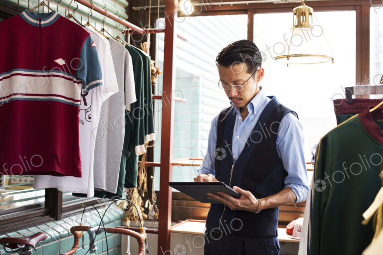 Japanese salesman standing in clothing store, looking at digital tablet.