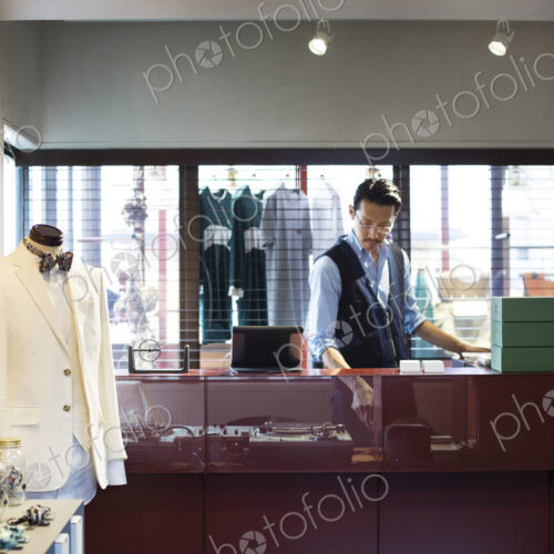 Japanese salesman with moustache wearing glasses standing at counter in clothing store. Japanese salesman with moustache wearing glasses standing at counter in clothing store.