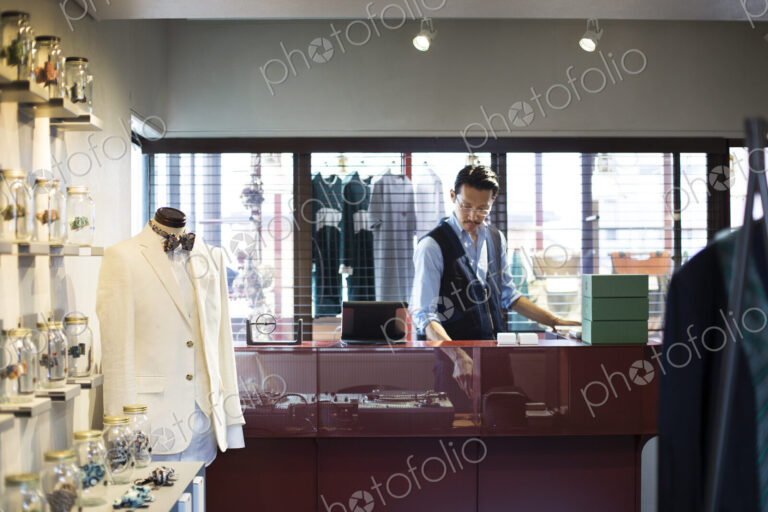 Japanese salesman with moustache wearing glasses standing at counter in clothing store.