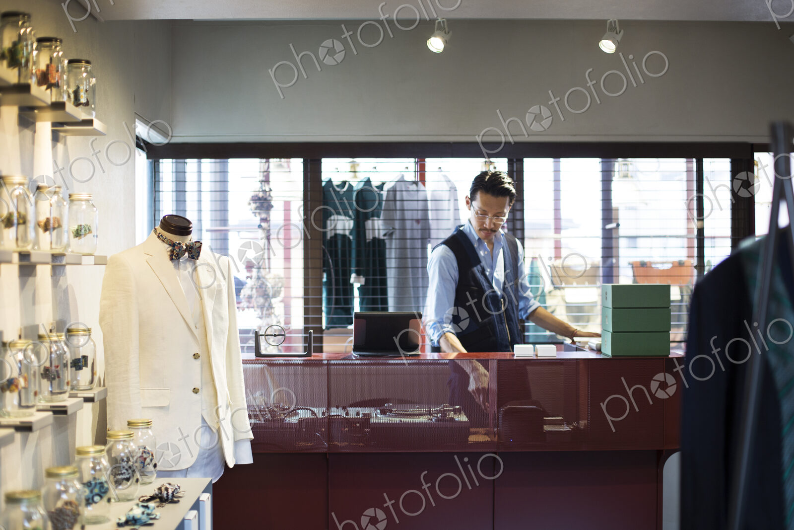 Japanese salesman with moustache wearing glasses standing at counter in clothing store.