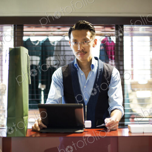 Japanese salesman with moustache wearing glasses standing at counter in clothing… Japanese salesman with moustache wearing glasses standing at counter in clothing…