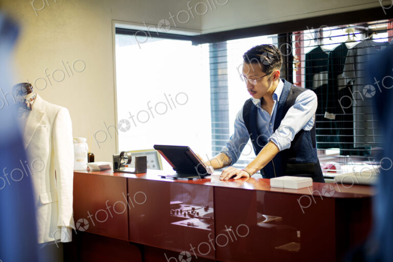 Japanese salesman with moustache wearing glasses standing at counter in clothing…