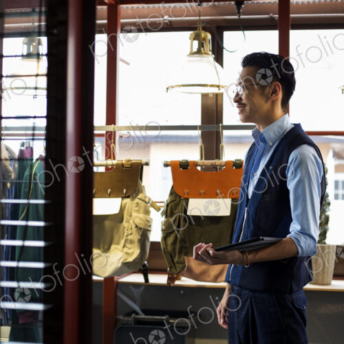 Japanese salesman with moustache wearing glasses standing in clothing store, holding… Japanese salesman with moustache wearing glasses standing in clothing store, holding…
