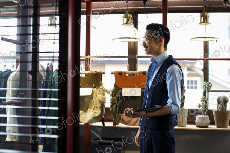 Japanese salesman with moustache wearing glasses standing in clothing store, holding…