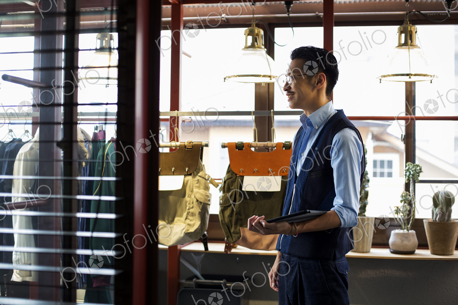 Japanese salesman with moustache wearing glasses standing in clothing store, holding…