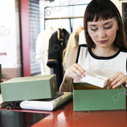 Japanese saleswoman standing at counter in clothing store, placing jewellery in green box. Japanese saleswoman standing at counter in clothing store, placing jewellery in green box.