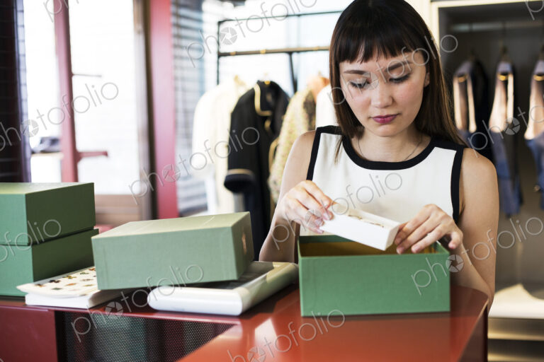 Japanese saleswoman standing at counter in clothing store, placing jewellery in green box.