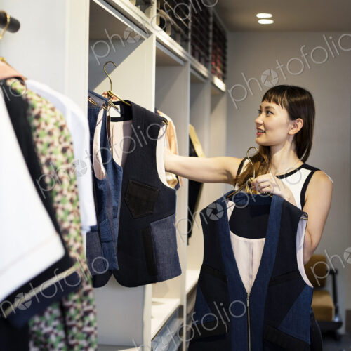 Japanese saleswoman standing in clothing store, hanging blue waistcoats on rail. Japanese saleswoman standing in clothing store, hanging blue waistcoats on rail.
