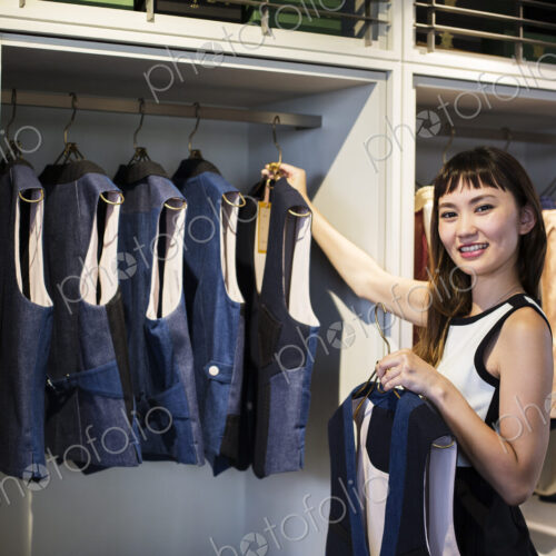 Japanese saleswoman standing in clothing store, hanging blue waistcoats on rail,… Japanese saleswoman standing in clothing store, hanging blue waistcoats on rail,…