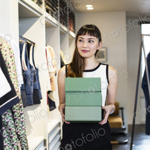 Japanese saleswoman standing in clothing store, holding stack of green boxes. Japanese saleswoman standing in clothing store, holding stack of green boxes.