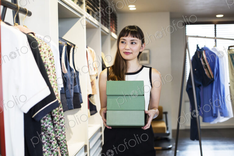 Japanese saleswoman standing in clothing store, holding stack of green boxes.