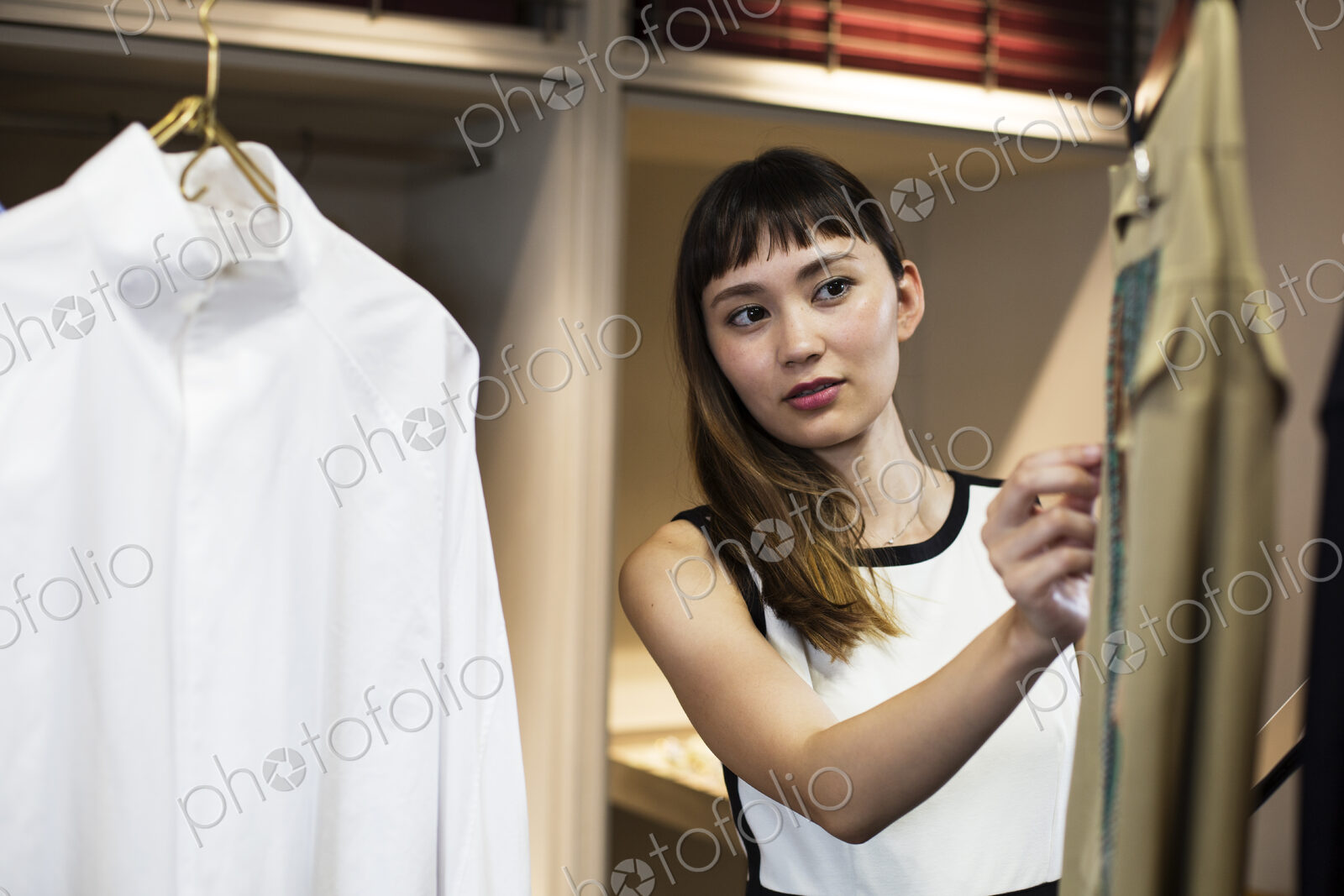 Japanese saleswoman standing in clothing store, looking at shirt.