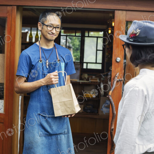 Japanese woman and man wearing blue apron and glasses standing outside a leather shop,… Japanese woman and man wearing blue apron and glasses standing outside a leather shop,…