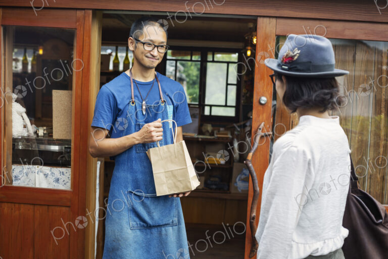 Japanese woman and man wearing blue apron and glasses standing outside a leather shop,…