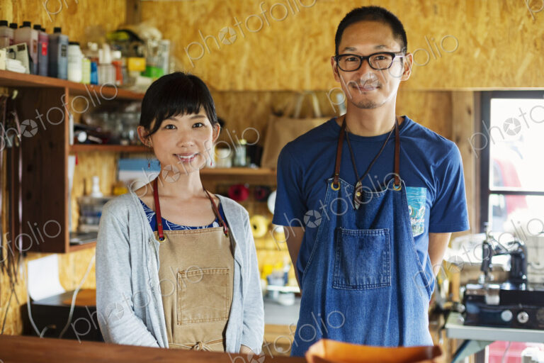 Japanese woman and man wearing blue apron standing in a leather shop, smiling at camera.