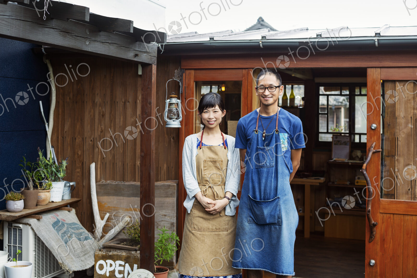 Japanese woman and man wearing blue apron standing outside a leather shop, smiling at…