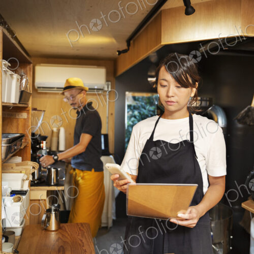 Japanese woman and man working in an Eco Cafe, preparing coffee, using mobile phone. Japanese woman and man working in an Eco Cafe, preparing coffee, using mobile phone.