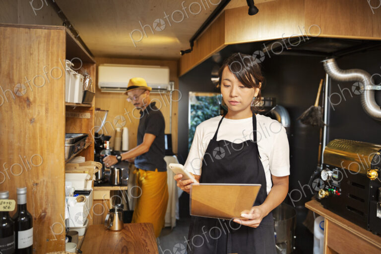 Japanese woman and man working in an Eco Cafe, preparing coffee, using mobile phone.
