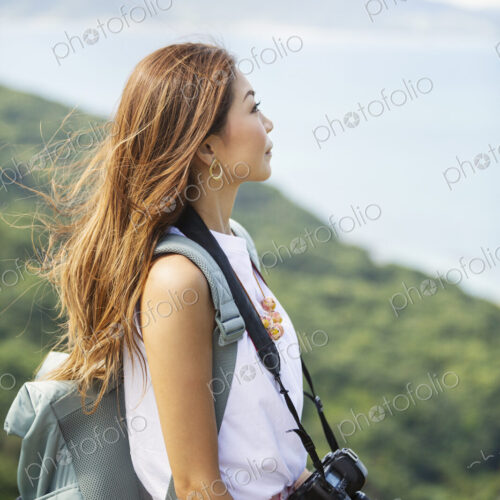 Japanese woman carrying backpack and holding camera standing on a cliff, ocean in the… Japanese woman carrying backpack and holding camera standing on a cliff, ocean in the…