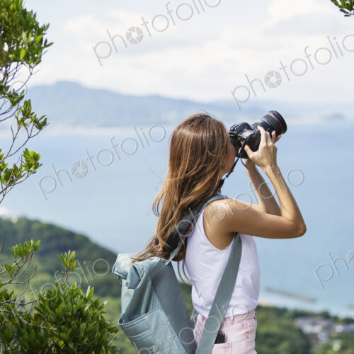 Japanese woman carrying backpack taking photograph on a cliff, ocean in the background. Japanese woman carrying backpack taking photograph on a cliff, ocean in the background.
