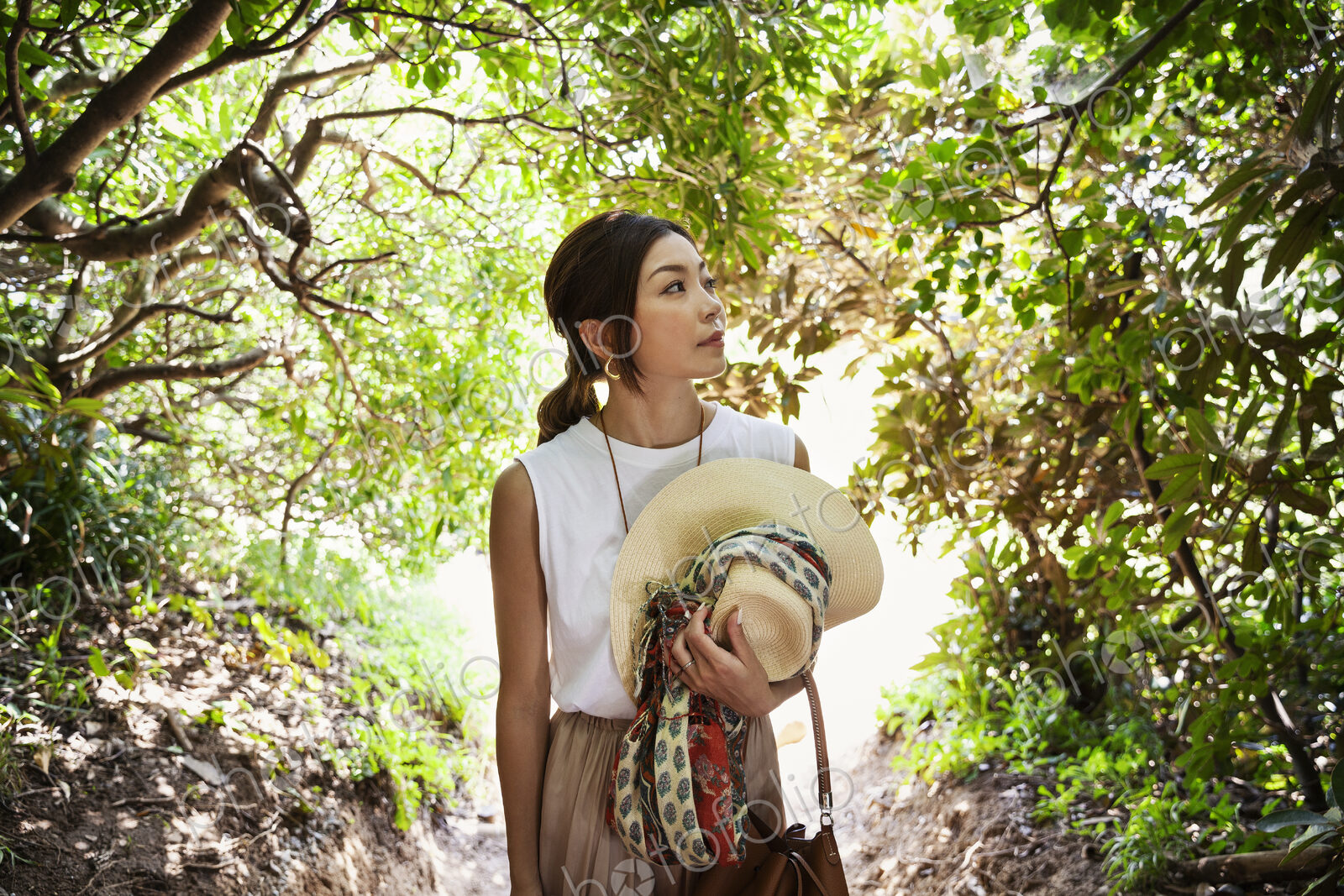 Japanese woman carrying hat hiking in a forest.