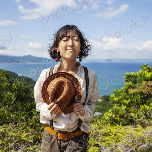 Japanese woman holding hat standing on a cliff, ocean in the background. Japanese woman holding hat standing on a cliff, ocean in the background.