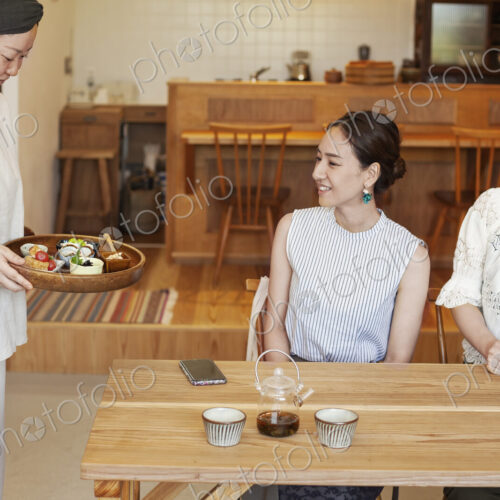 Japanese woman serving two female customers in a vegetarian cafe. Japanese woman serving two female customers in a vegetarian cafe.