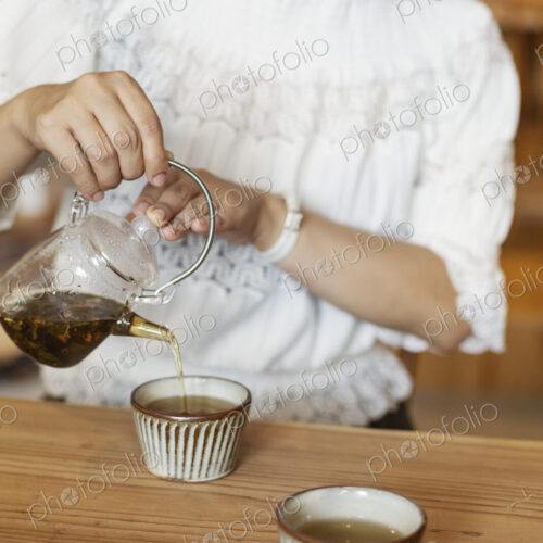 Japanese woman sitting at a table in a vegetarian cafe, pouring tea. Japanese woman sitting at a table in a vegetarian cafe, pouring tea.
