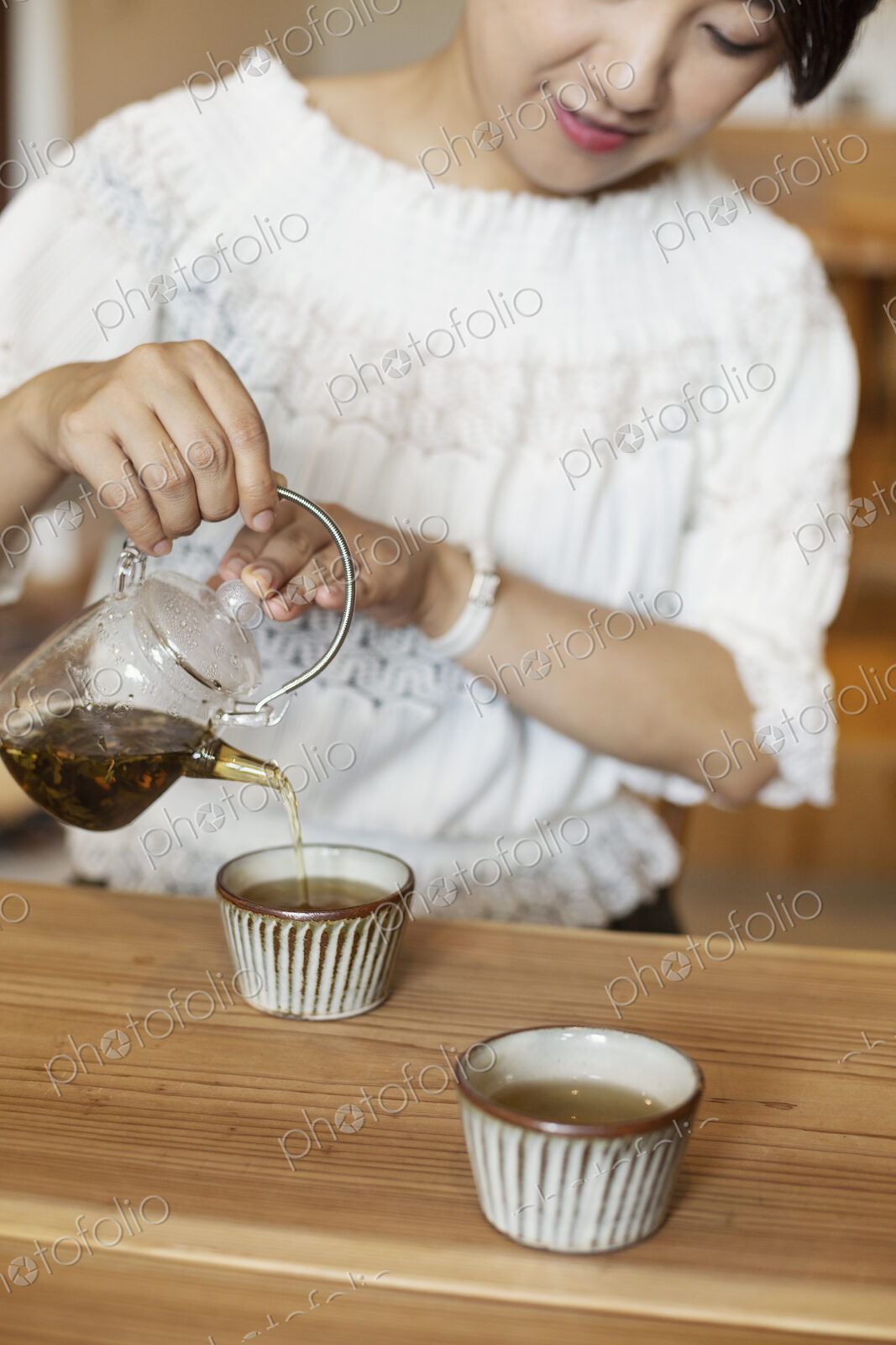 Japanese woman sitting at a table in a vegetarian cafe, pouring tea.