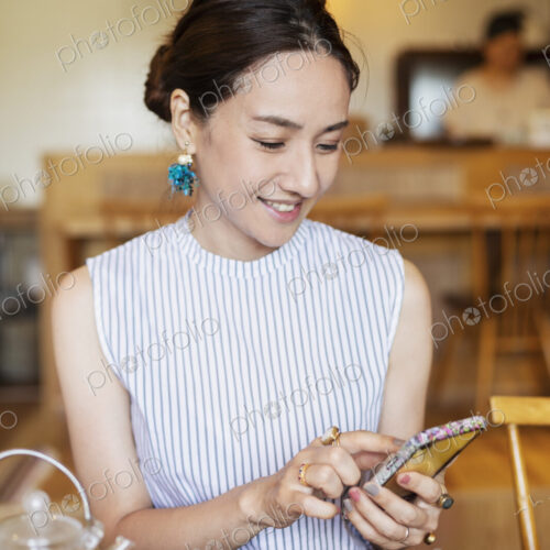 Japanese woman sitting at a table in a vegetarian cafe, using mobile phone. Japanese woman sitting at a table in a vegetarian cafe, using mobile phone.