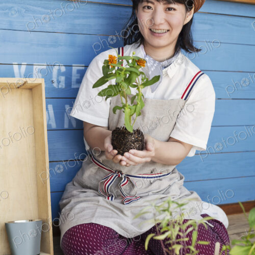 Japanese woman sitting outside a farm shop, planting flowers into flower pots. Japanese woman sitting outside a farm shop, planting flowers into flower pots.