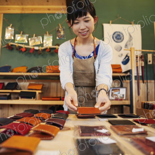 Japanese woman standing at a table, working in a leather shop.