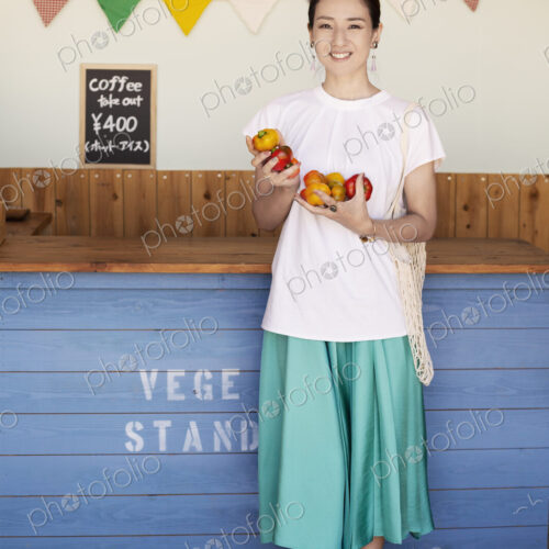 Japanese woman standing in a farm shop, holding vegetables, smiling at camera. Japanese woman standing in a farm shop, holding vegetables, smiling at camera.